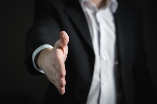 About Close-up of a businessman extending hand for a handshake, symbolizing agreement and partnership.